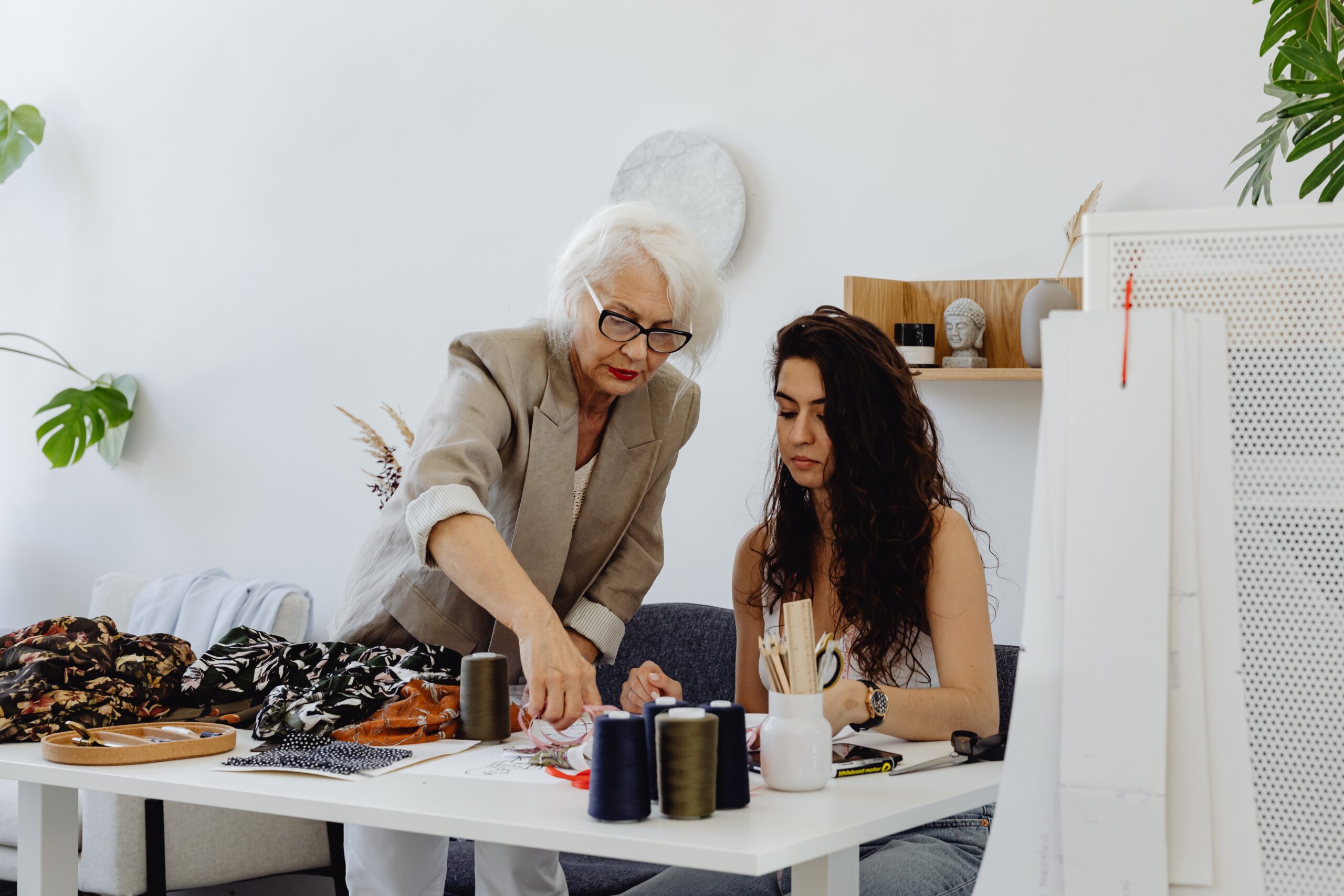 An elderly woman and her granddaughter looking at the table with sewing threads and fabrics