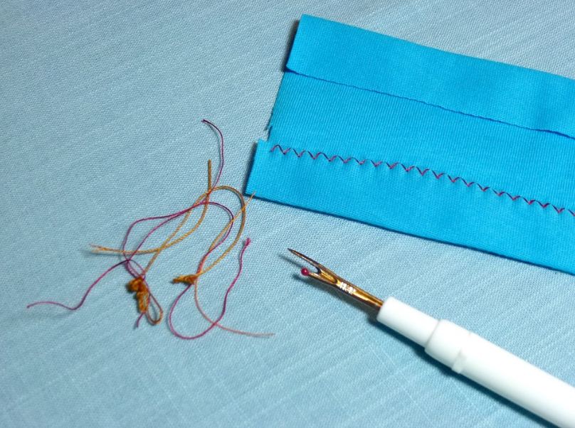 A blue seam ripper along with a piece of cloth