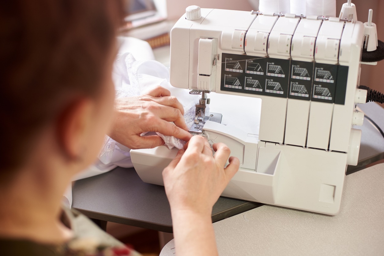 Woman in sewing studio: sewing with serger, overlocker. Fashion designers atelier. Close up view of sewing machine.